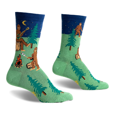 front view of two socks, one on top of the other, featuring a pattern of a bigfoot, a campfire, a forest, and a moon.  the socks are green with blue cuffs.