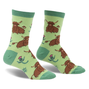 a pair of socks with a green background.  the socks have a repeated pattern of brown hairy cows and pink thistle flowers. the socks are shown at a slight angle, with the toes of the socks facing the viewer. the socks are on a white background.