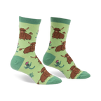 Pair of crew socks featuring a repeating pattern of brown Highland cows and pink thistles on a light green background.