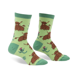 Pair of crew socks featuring a repeating pattern of brown Highland cows and pink thistles on a light green background.