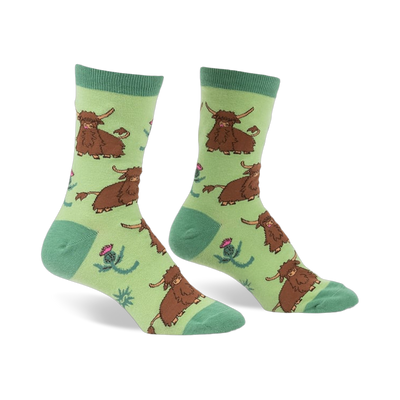 Pair of crew socks featuring a repeating pattern of brown Highland cows and pink thistles on a light green background.