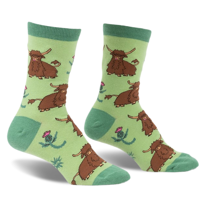 a pair of socks with a green background.  the socks have a repeated pattern of brown hairy cows and pink thistle flowers. the socks are shown at a slight angle, with the toes of the socks facing the viewer. the socks are on a white background.