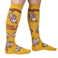Lifestyle shot: Model wearing a pair of mustard yellow knee-high socks with possum designs.