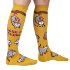 Lifestyle shot: Model wearing a pair of mustard yellow knee-high socks with possum designs.