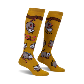 Pair of mustard yellow knee-high socks with playful possum illustrations and the phrase 'Hang in there'.