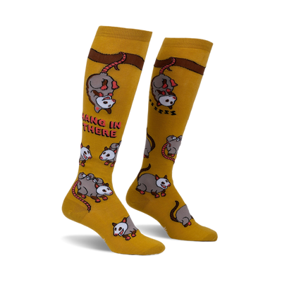 Pair of mustard yellow knee-high socks with playful possum illustrations and the phrase 'Hang in there'.