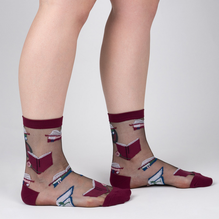 Lifestyle shot showing the socks on a person's legs. The socks are sheer and feature a pattern of books and roses.