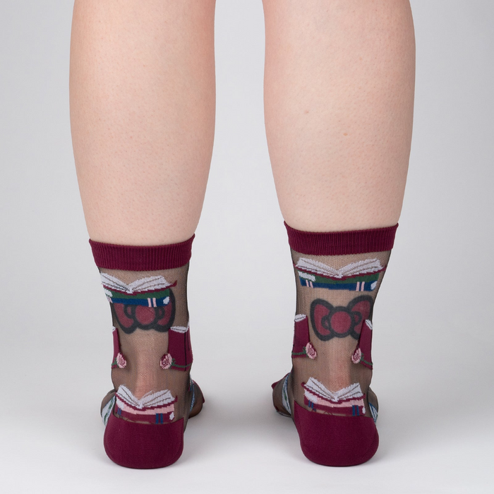 Rear view of a person's legs wearing the sheer socks. The pattern of books and roses is visible.