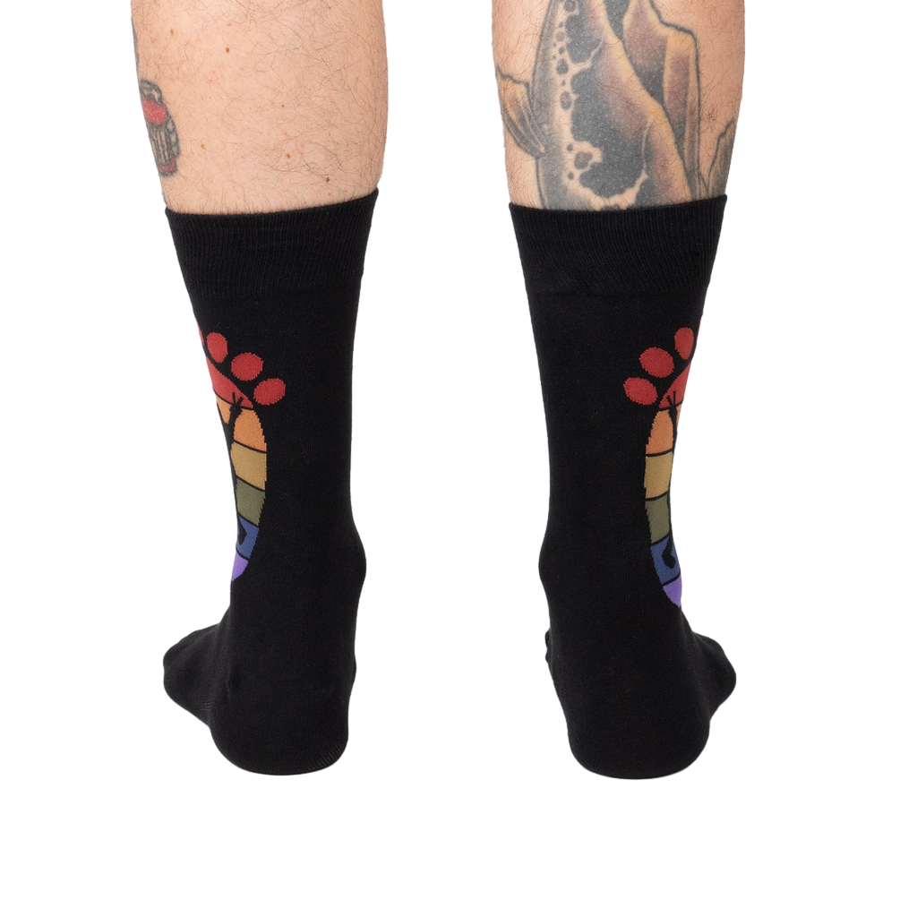 Rear view of the black 'Squatch and Learn' socks, highlighting the full rainbow footprint design on both socks.