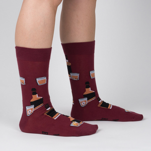 Lifestyle shot showing the Whiskey Business socks on a person's legs.  Burgundy socks with whiskey bottle and glass design.