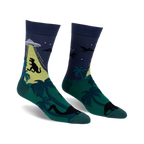 Crew socks in dark blue, green, and yellow. The design features a T-Rex, UFO, palm trees, and pterodactyls.