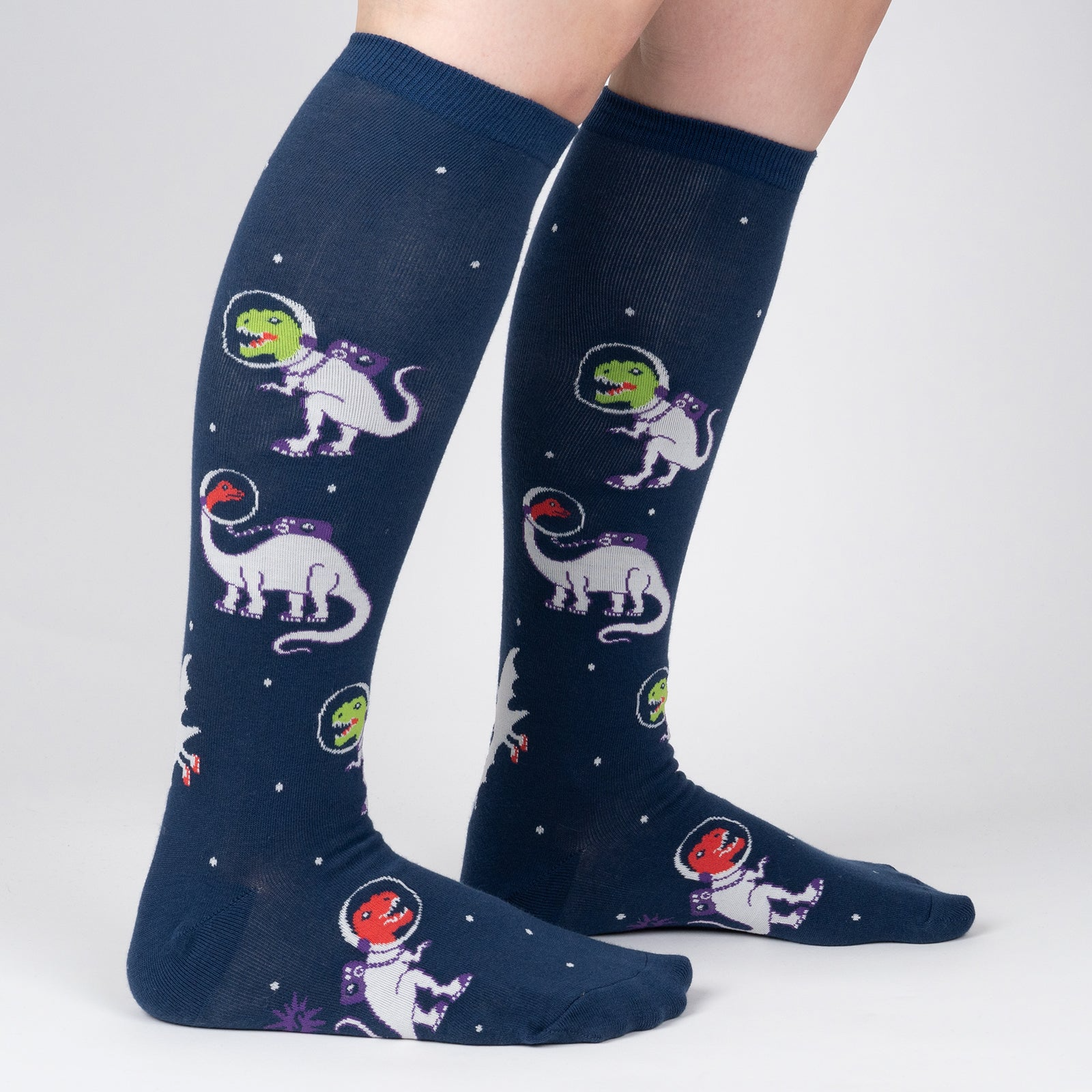 Lifestyle shot showing 'I Need Space' socks on a person's legs. The socks are knee-high and feature a space-themed pattern with dinosaurs.