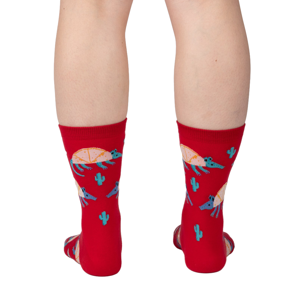 Back view of a person wearing a pair of red crew socks with armadillo and cacti print.