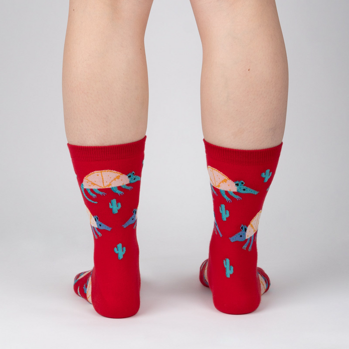 Back view of a person wearing a pair of red crew socks with armadillo and cacti print.