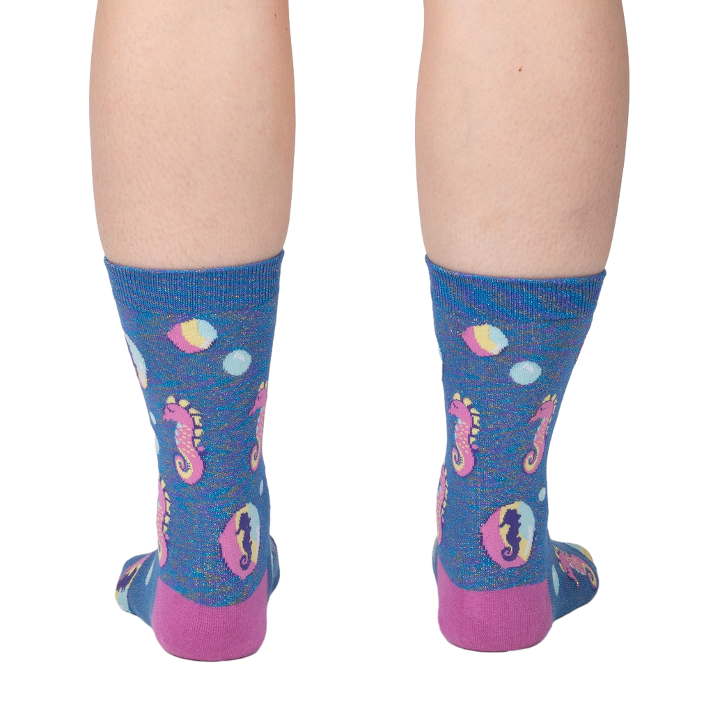 Back view of model wearing a pair of blue crew socks with seahorse and bubble design.