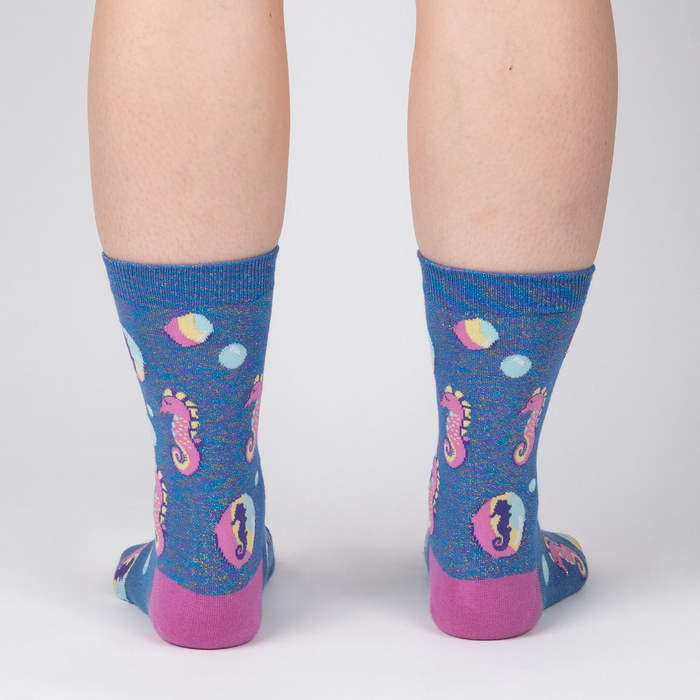 Back view of model wearing a pair of blue crew socks with seahorse and bubble design.