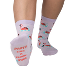 Close-up of a person's feet showcasing the 'Party Like A Flock Star' text on the sole of a lavender crew sock, accompanied by a flamingo design.