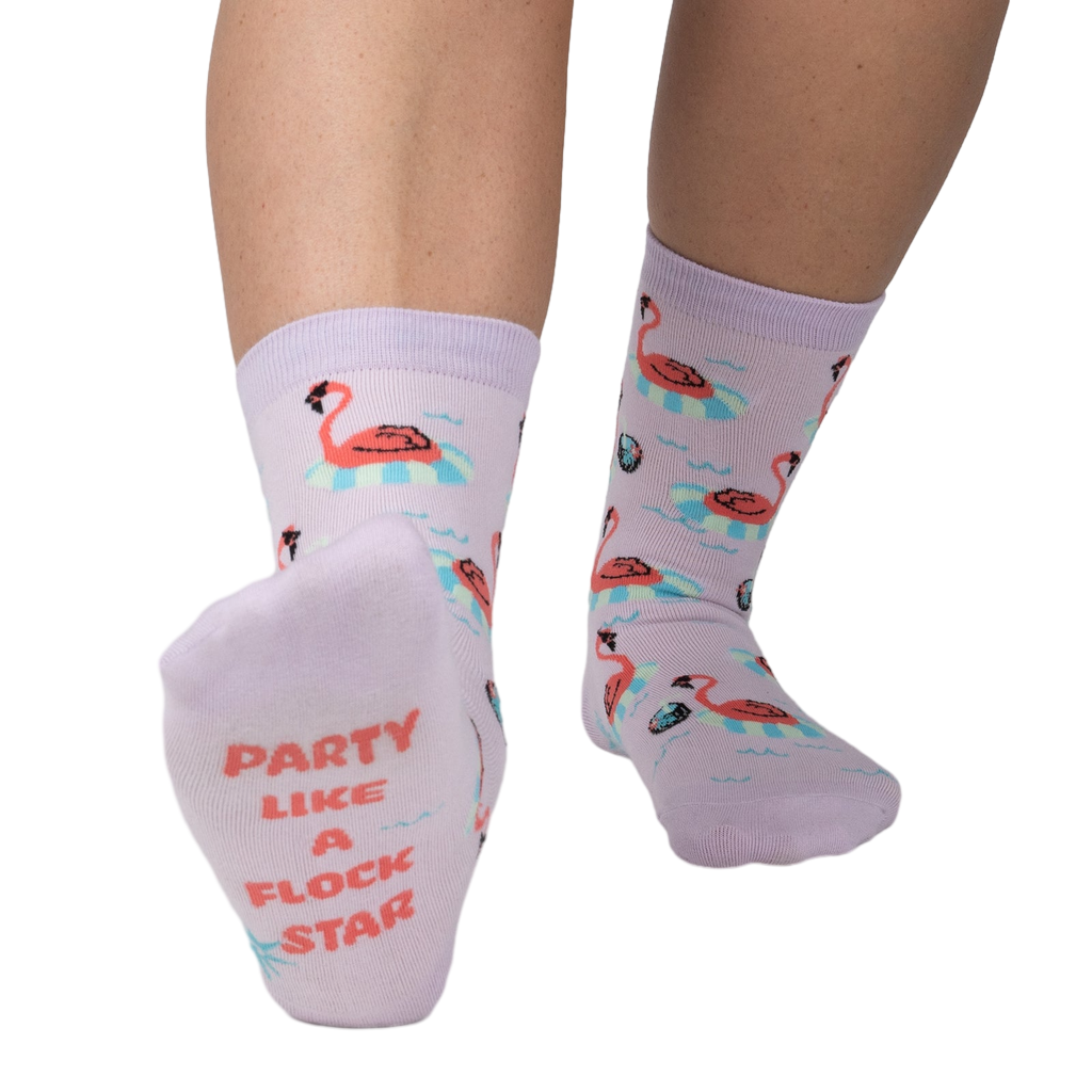 Close-up of a person's feet showcasing the 'Party Like A Flock Star' text on the sole of a lavender crew sock, accompanied by a flamingo design.