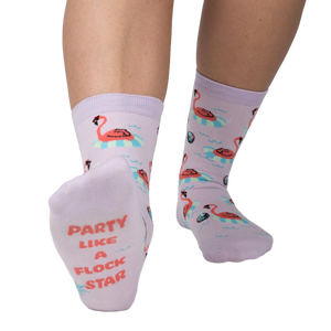 Close-up of a person's feet showcasing the 'Party Like A Flock Star' text on the sole of a lavender crew sock, accompanied by a flamingo design.