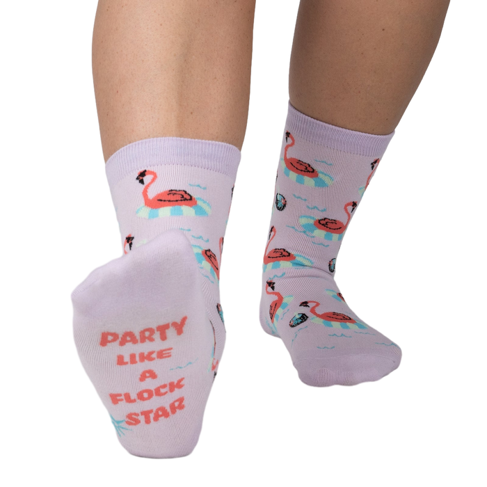 Close-up of a person's feet showcasing the 'Party Like A Flock Star' text on the sole of a lavender crew sock, accompanied by a flamingo design.