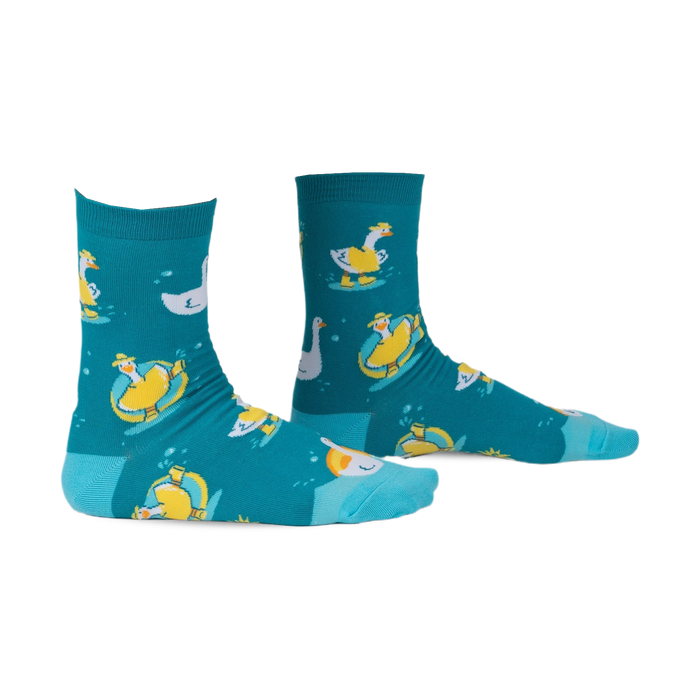 Pair of teal crew socks with a whimsical pattern of geese floating on inner tubes and swimming. Yellow and white geese on teal background.
