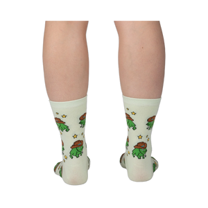 Back view of legs wearing pale crew socks featuring a pattern of green pixel frogs in brown cowboy hats and yellow stars.