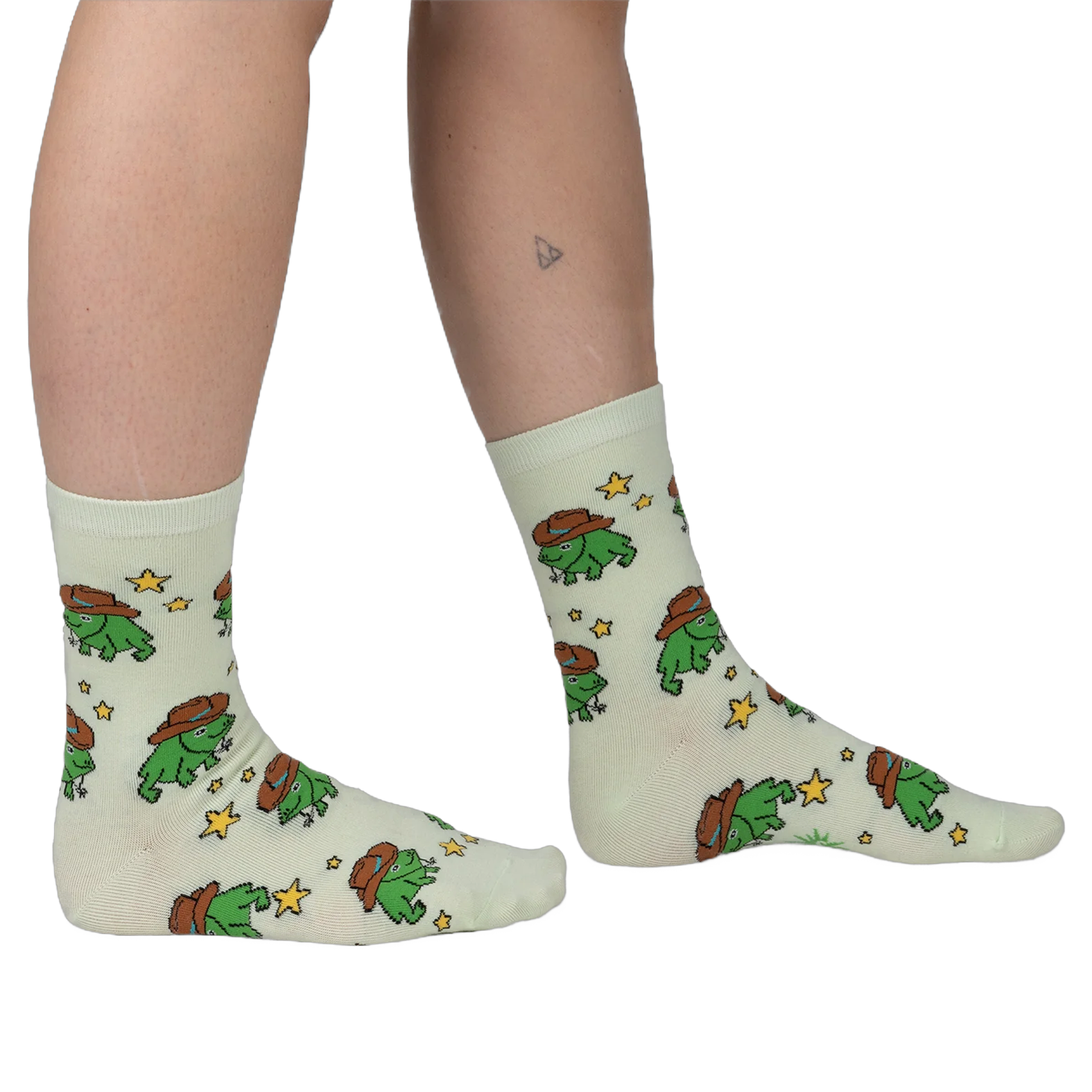 Person wearing pale mint crew socks featuring a repeating pattern of green pixel-art frogs in brown cowboy hats and stars.