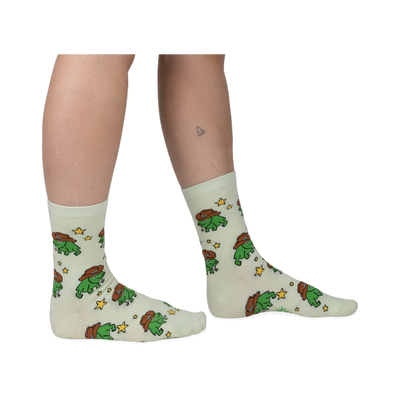 Person wearing pale mint crew socks featuring a repeating pattern of green pixel-art frogs in brown cowboy hats and stars.