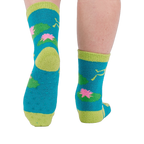 A person's legs and feet, viewed from behind, wearing the fuzzy teal blue slipper socks with visible grippers on the soles.