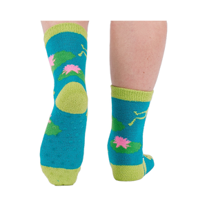 A person's legs and feet, viewed from behind, wearing the fuzzy teal blue slipper socks with visible grippers on the soles.