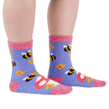 Person wearing fuzzy periwinkle slipper socks with bee, mushroom, and flower patterns, side view.