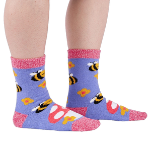 Person wearing fuzzy periwinkle slipper socks with bee, mushroom, and flower patterns, side view.