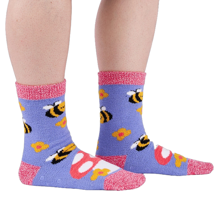 Person wearing fuzzy periwinkle slipper socks with bee, mushroom, and flower patterns, side view.
