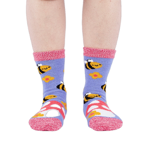 Person wearing fuzzy periwinkle slipper socks with bee, mushroom, and flower patterns, front view.