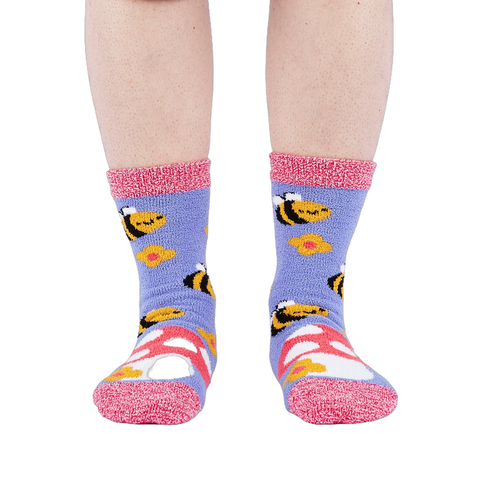 Person wearing fuzzy periwinkle slipper socks with bee, mushroom, and flower patterns, front view.