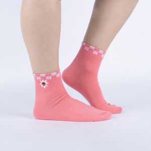 Lifestyle shot showing the socks on a person's feet. The socks are pink with a white and pink checkered cuff and embroidered daisy with an eye in the center.