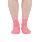 Another lifestyle shot showing the socks on a person's feet from a different angle. The socks are pink with a white and pink checkered cuff and embroidered daisy with an eye in the center.