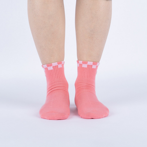 Another lifestyle shot showing the socks on a person's feet from a different angle. The socks are pink with a white and pink checkered cuff and embroidered daisy with an eye in the center.