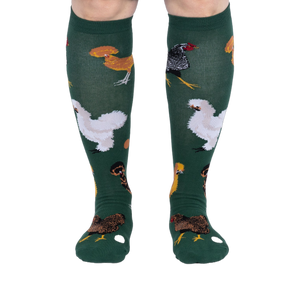 Person wearing dark green knee-high socks patterned with various chickens and eggs, standing, front view.