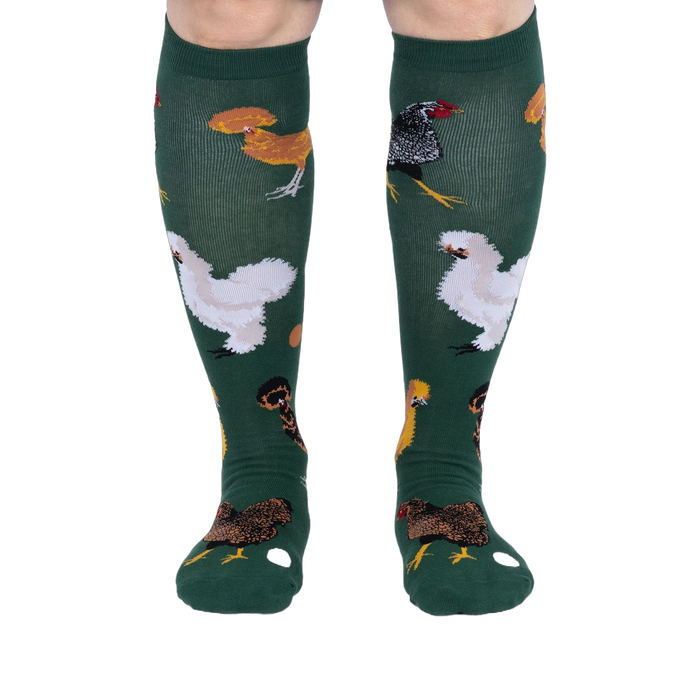 Person wearing dark green knee-high socks patterned with various chickens and eggs, standing, front view.