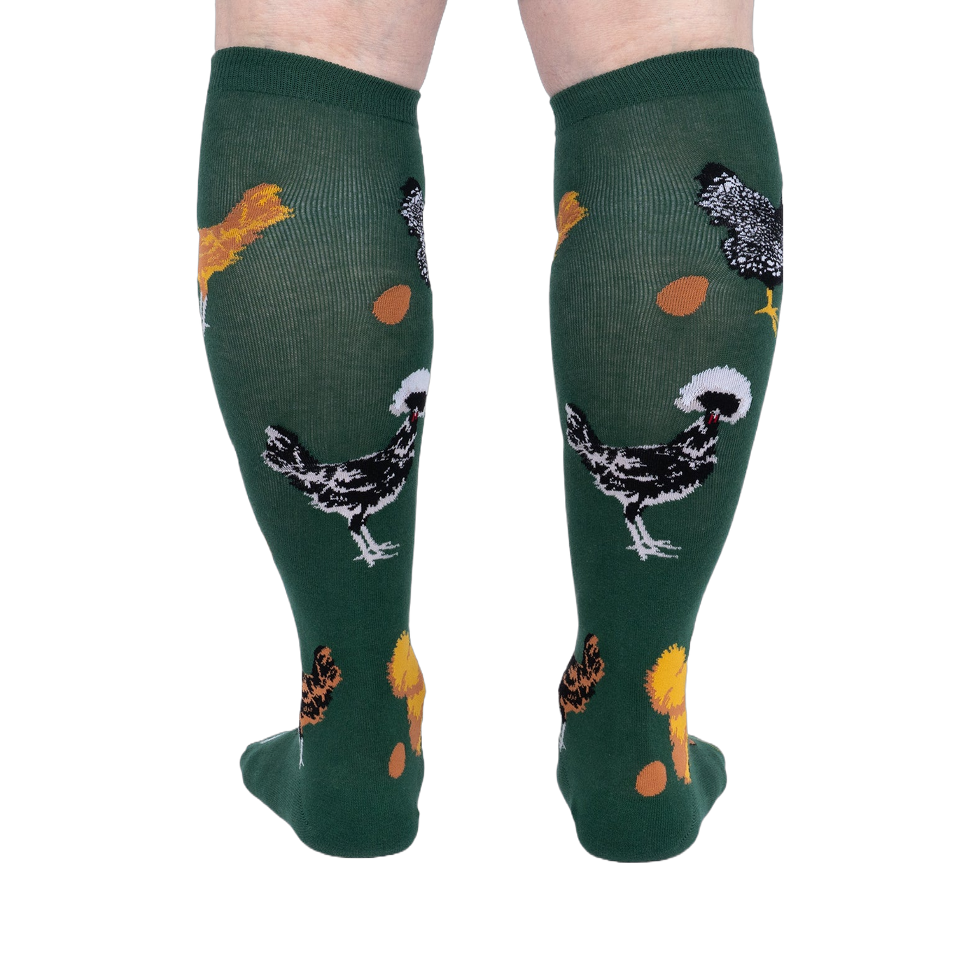 Person wearing dark green knee-high socks patterned with various chickens and eggs, standing, back view.