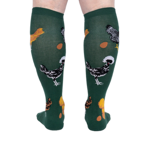 Person wearing dark green knee-high socks patterned with various chickens and eggs, standing, back view.