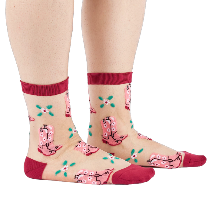 A person's legs and feet, wearing sheer pink cowboy boot socks from the side. Legs are bare against a white background.