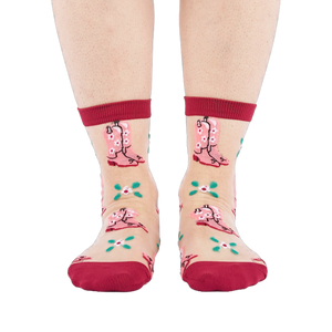 A person's legs and feet, wearing sheer pink cowboy boot socks, viewed from the front against a white background.