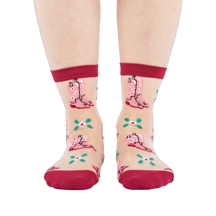 A person's legs and feet, wearing sheer pink cowboy boot socks, viewed from the front against a white background.