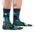 Person's lower legs with hairy calves and tattoos, wearing dark green cryptid socks, seen from the side.