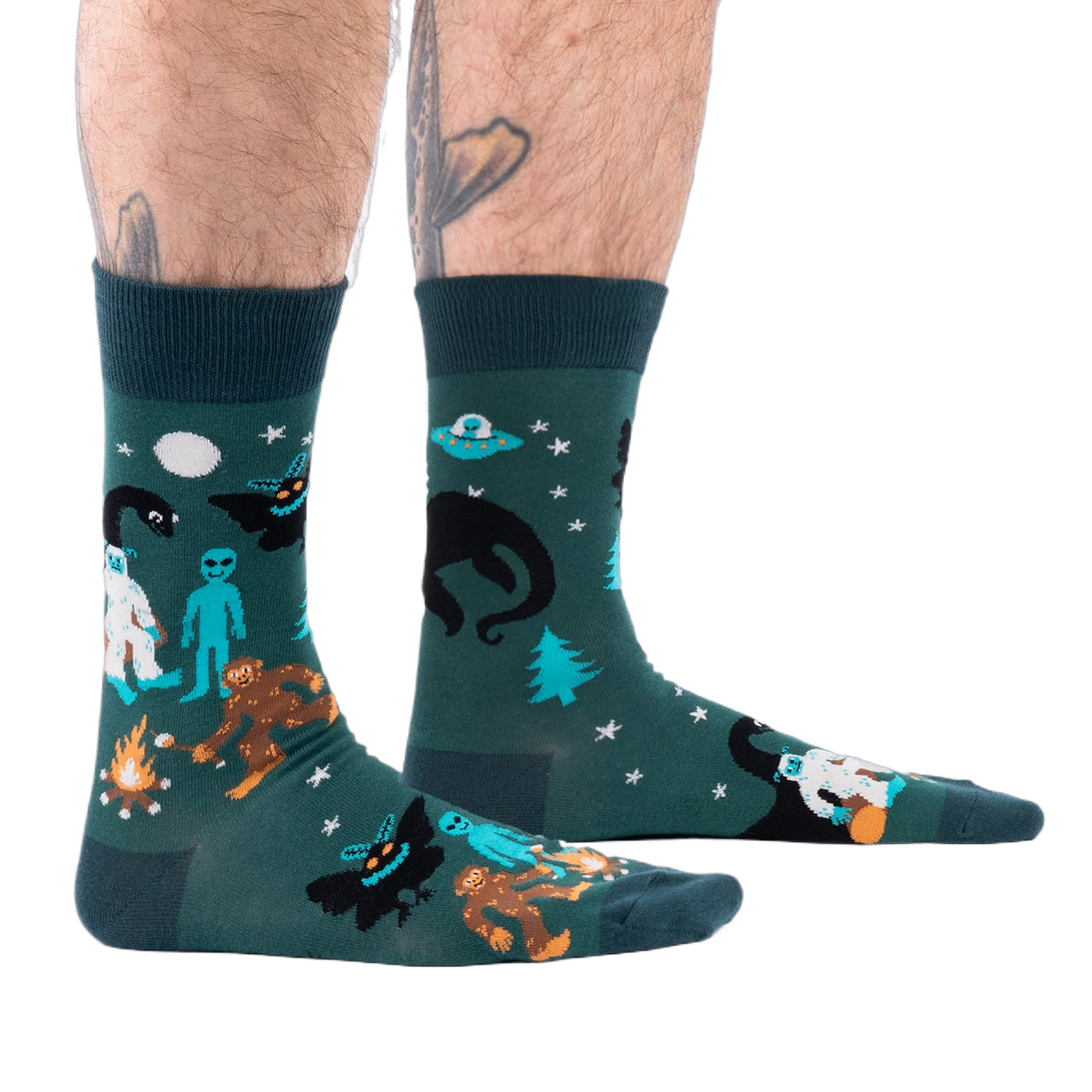 Person's lower legs with hairy calves and tattoos, wearing dark green cryptid socks, seen from the side.