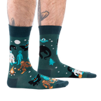 Person's lower legs with hairy calves and tattoos, wearing dark green cryptid socks, seen from the side.