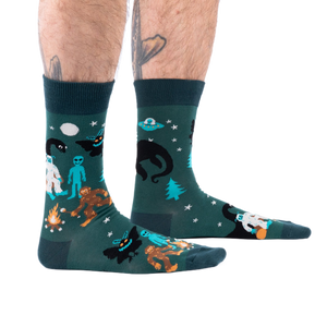 Person's lower legs with hairy calves and tattoos, wearing dark green cryptid socks, seen from the side.