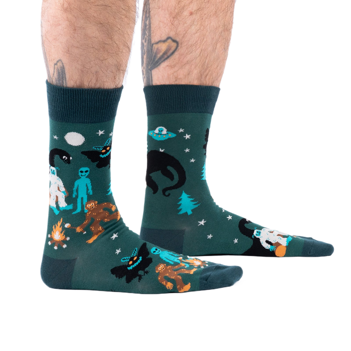 Person's lower legs with hairy calves and tattoos, wearing dark green cryptid socks, seen from the side.